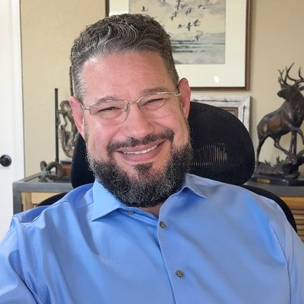 Miles D. Kramer, a bearded man in a light blue shirt, seated in his office.